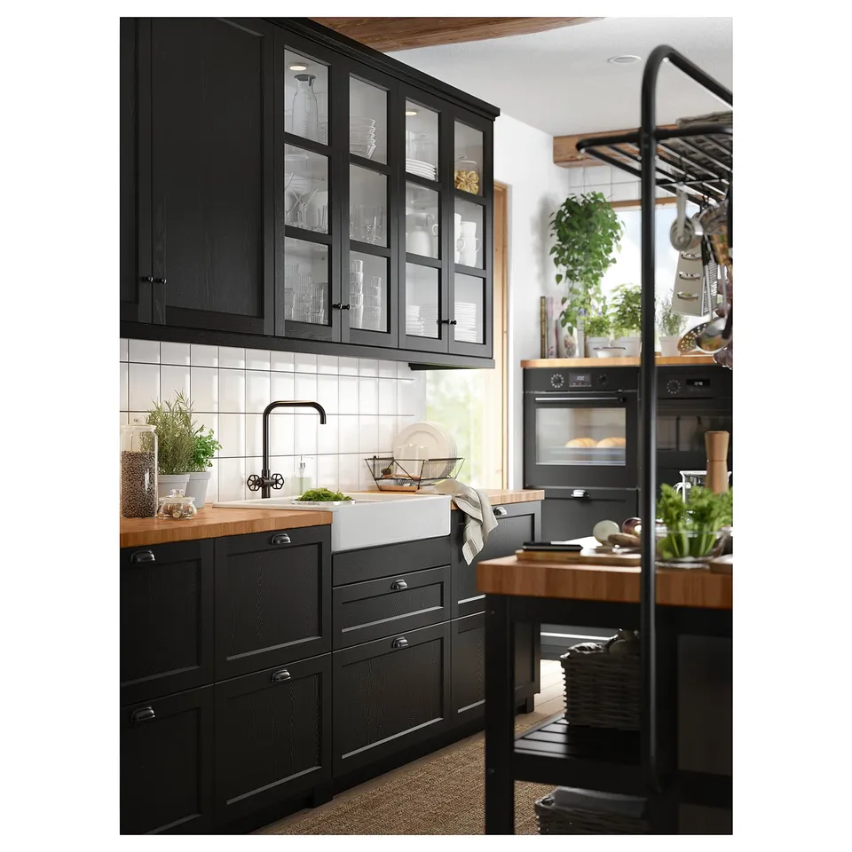 Modern kitchen with black cabinets and a black rustic tap, wooden countertop, and glass-fronted cabinets, featuring greenery and cookware.
