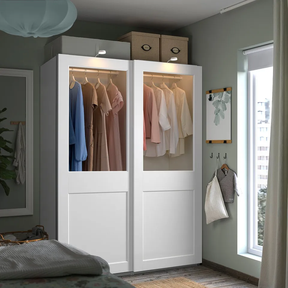 Modern bedroom with large white PAX wardrobe, sliding glass doors, and neat clothes.
