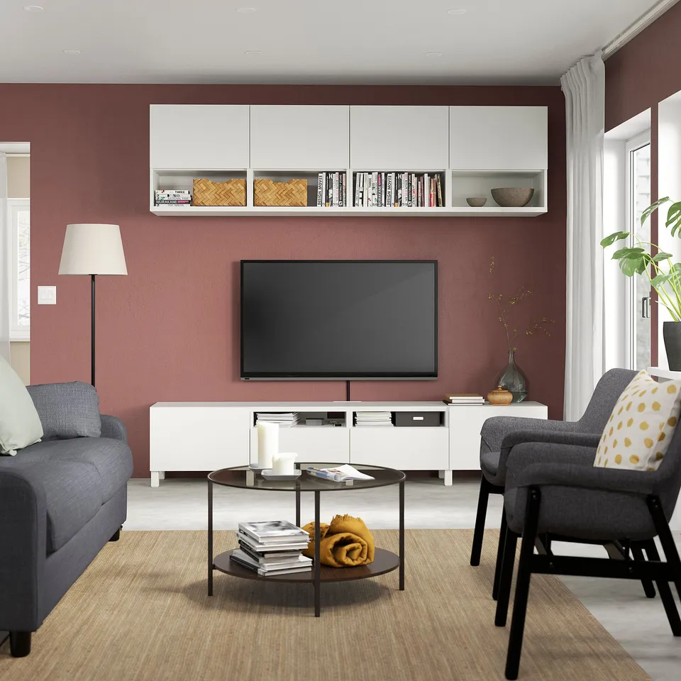 Modern living room with red walls, white cabinets, tv, grey sofa, armchair, coffee table, carpet, lamp.