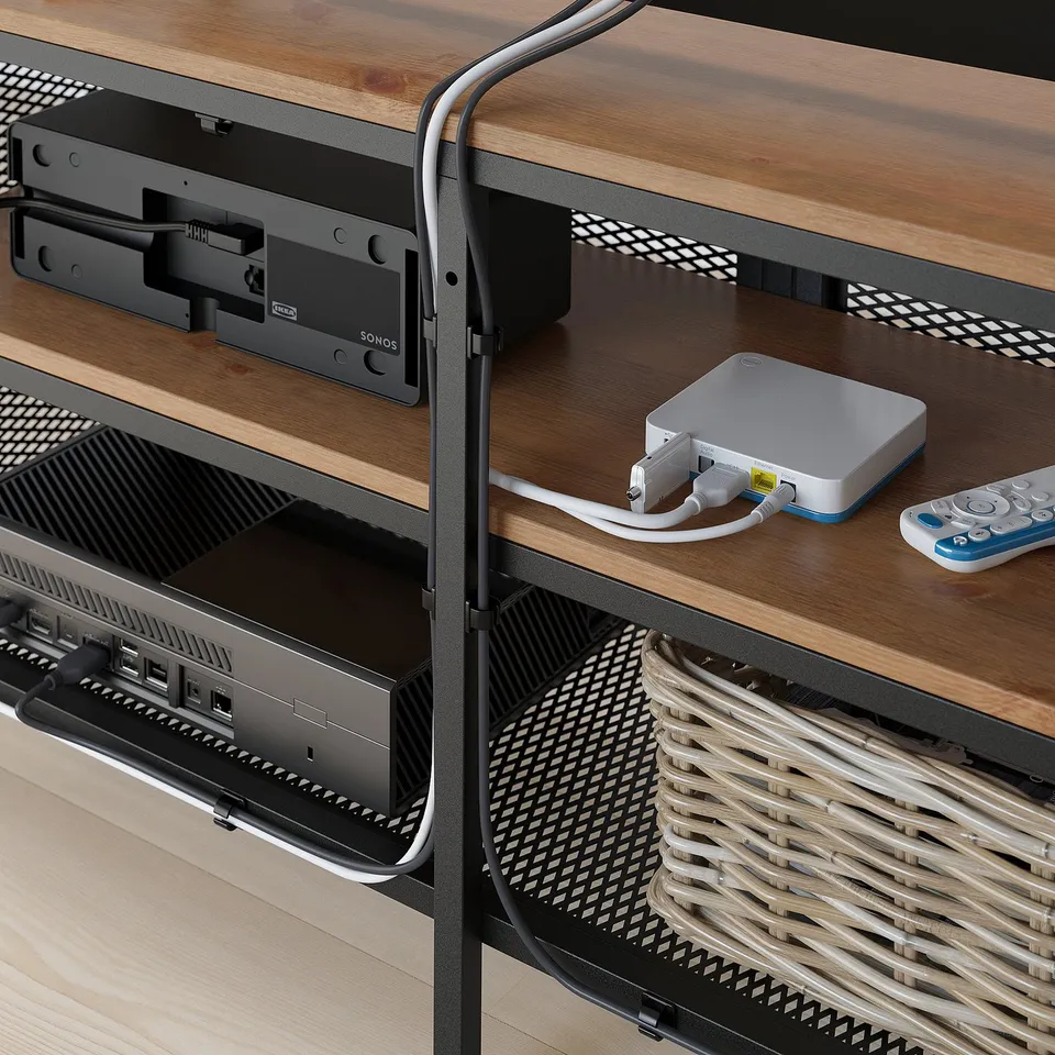 Wooden tv stand with metal mesh shelves, housing electronic devices. Black cables connect equipment, with remote controls ready for use.