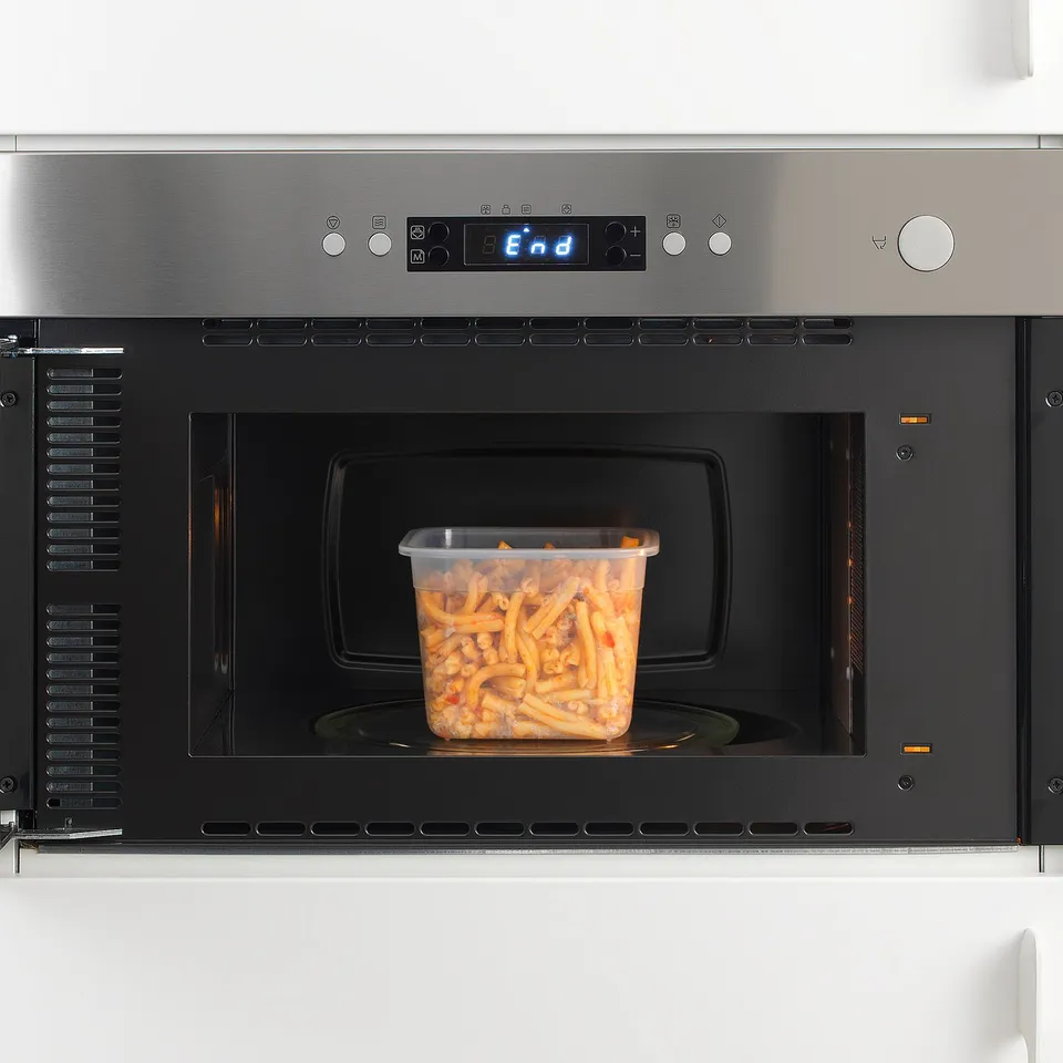 Clear plastic container filled with orange food in microwave, heating.