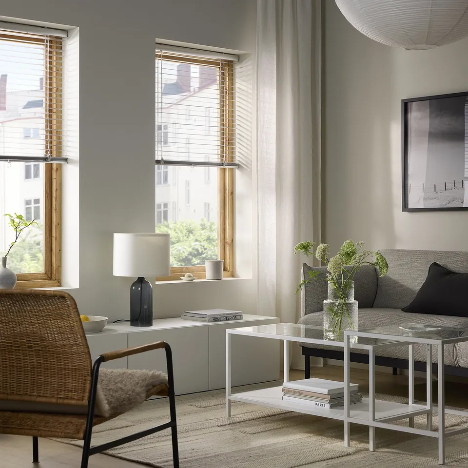 Cosy living room with VECKLARFLY blinds. Light-grey sofa, woven chair, and white coffee table. Blinds brighten space, controlling privacy.
