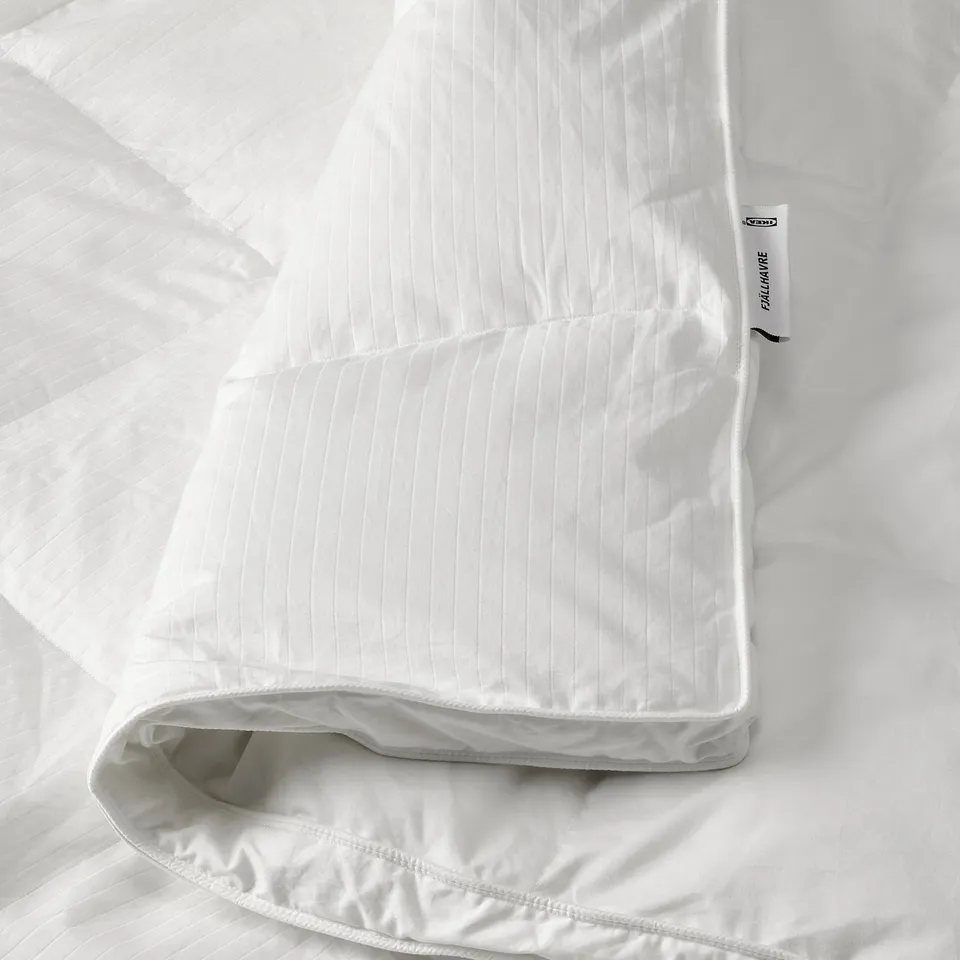 A luxurious white down duvet by ikea FJÄLLHAVRE, neatly folded with stitched side walls for enhanced warmth and fluffiness.