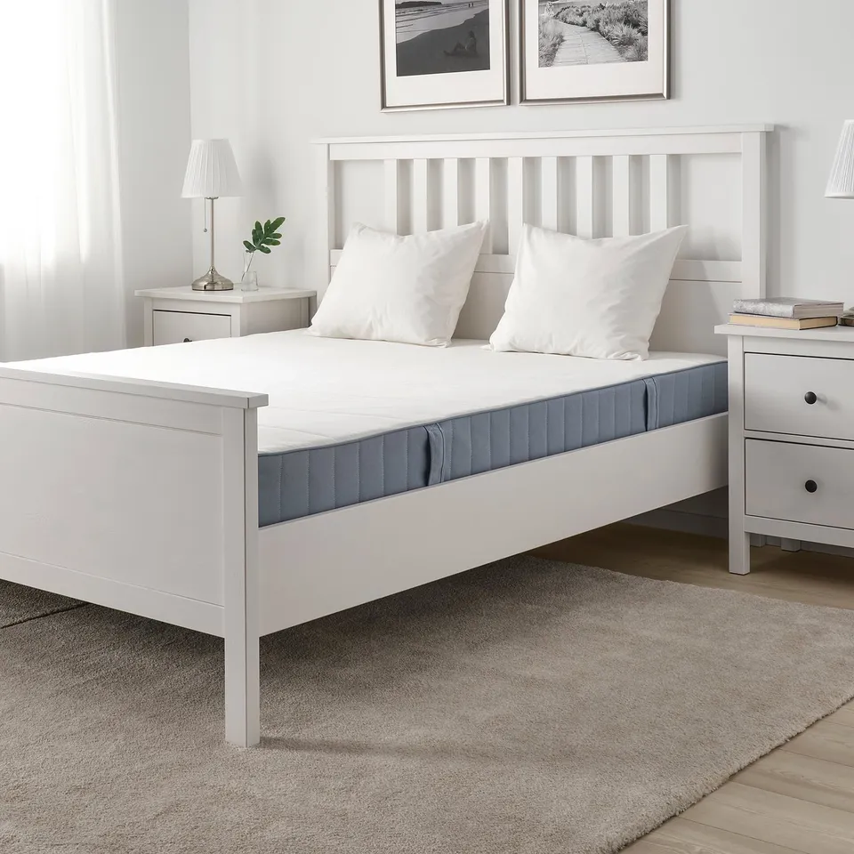 VESTMARKA bed with firm mattress, pillows, grey rug, wooden floor, nightstands with lamps.