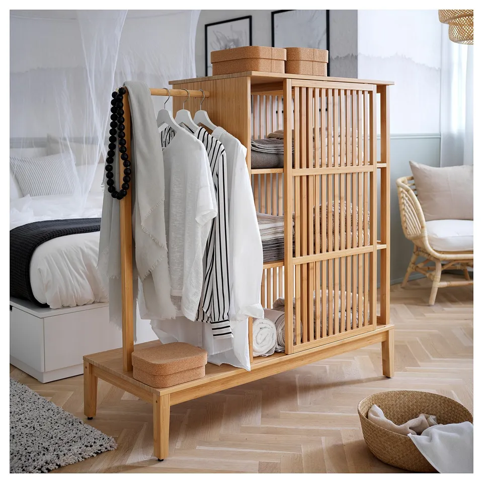 A wooden NORDKISA wardrobe with hooks and shelves, displaying clothes and organiser boxes. Its placed in a light, minimalist bedroom.
