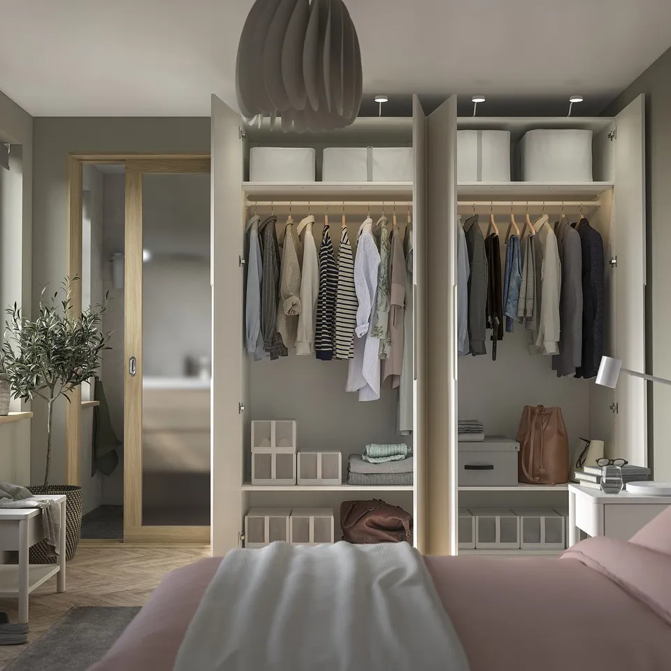 Modern bedroom with open PAX wardrobe displaying clothes, bags, and storage boxes. A cosy bed with pink sheets is in the foreground.