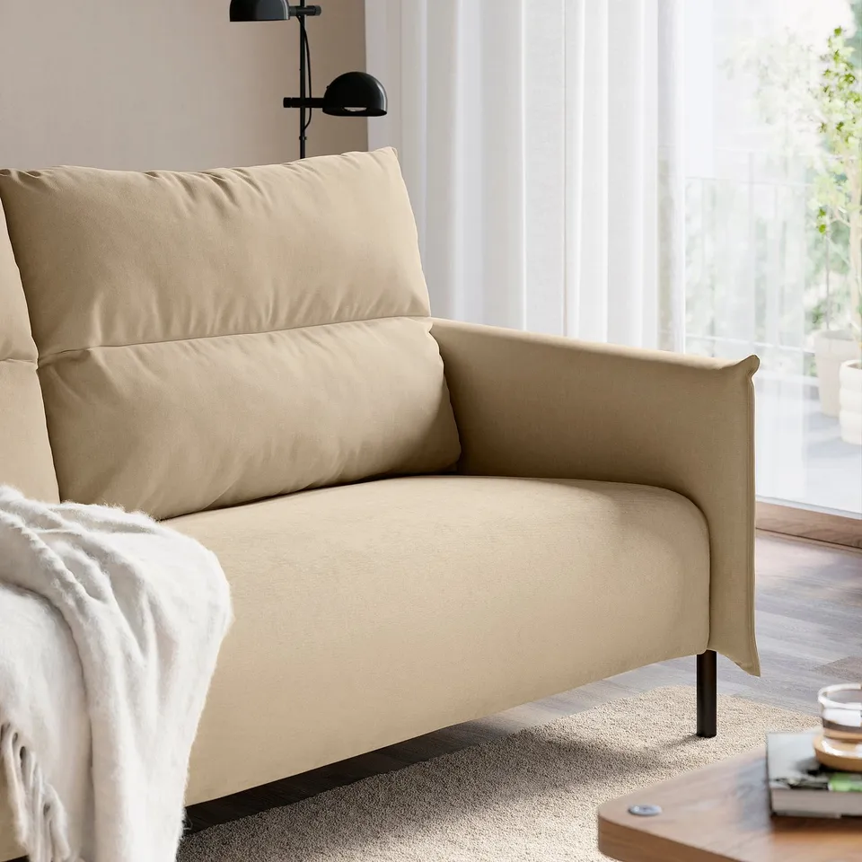 Beige armchair with cushions by window for relaxation.