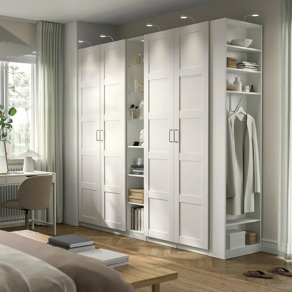 White IKEA PAX wardrobe, tall with open/closed storage, shelves, hanging space in bright room.