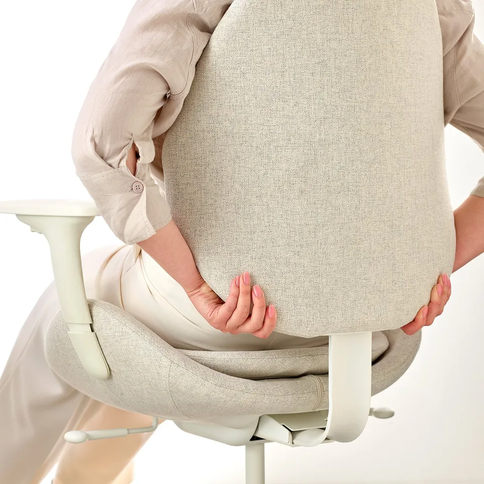 Person adjusting lumbar support on beige ergonomic office chair.