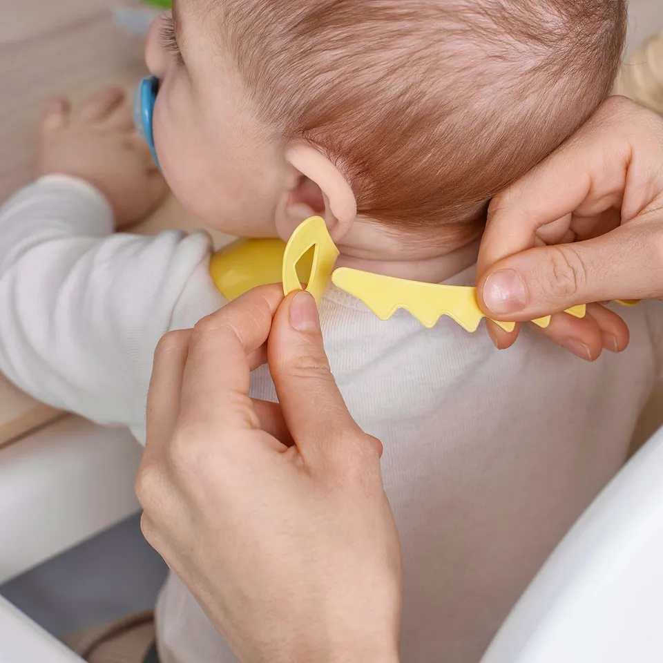 Adult helping baby wear yellow bib with food pocket, adjustable for meals.