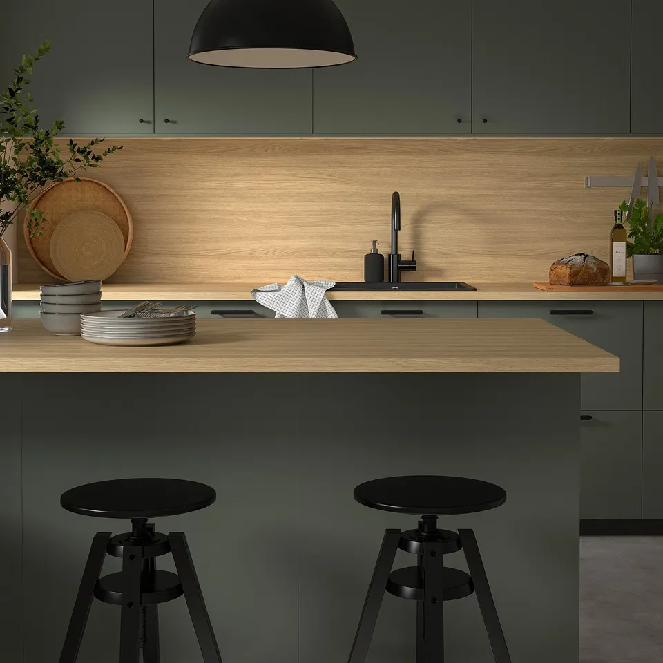 Modern kitchen island with EKBACKEN light wood countertop, black bar stools and green cabinets, featuring a sleek, clean design.