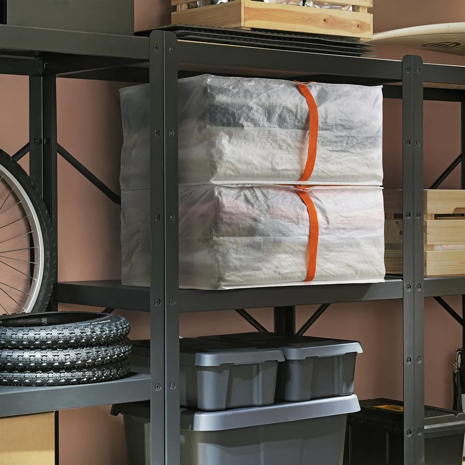 Black metal PÄRKLA shelves holding large white storage bags with orange straps, grey plastic bins, and bike tyres.
