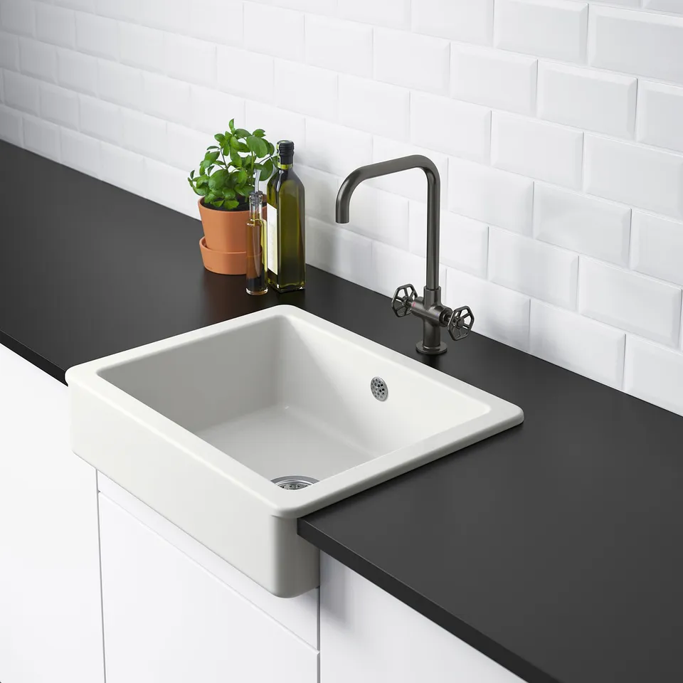 Single white kitchen sink with modern tap, black countertop, plant, and oil bottle.