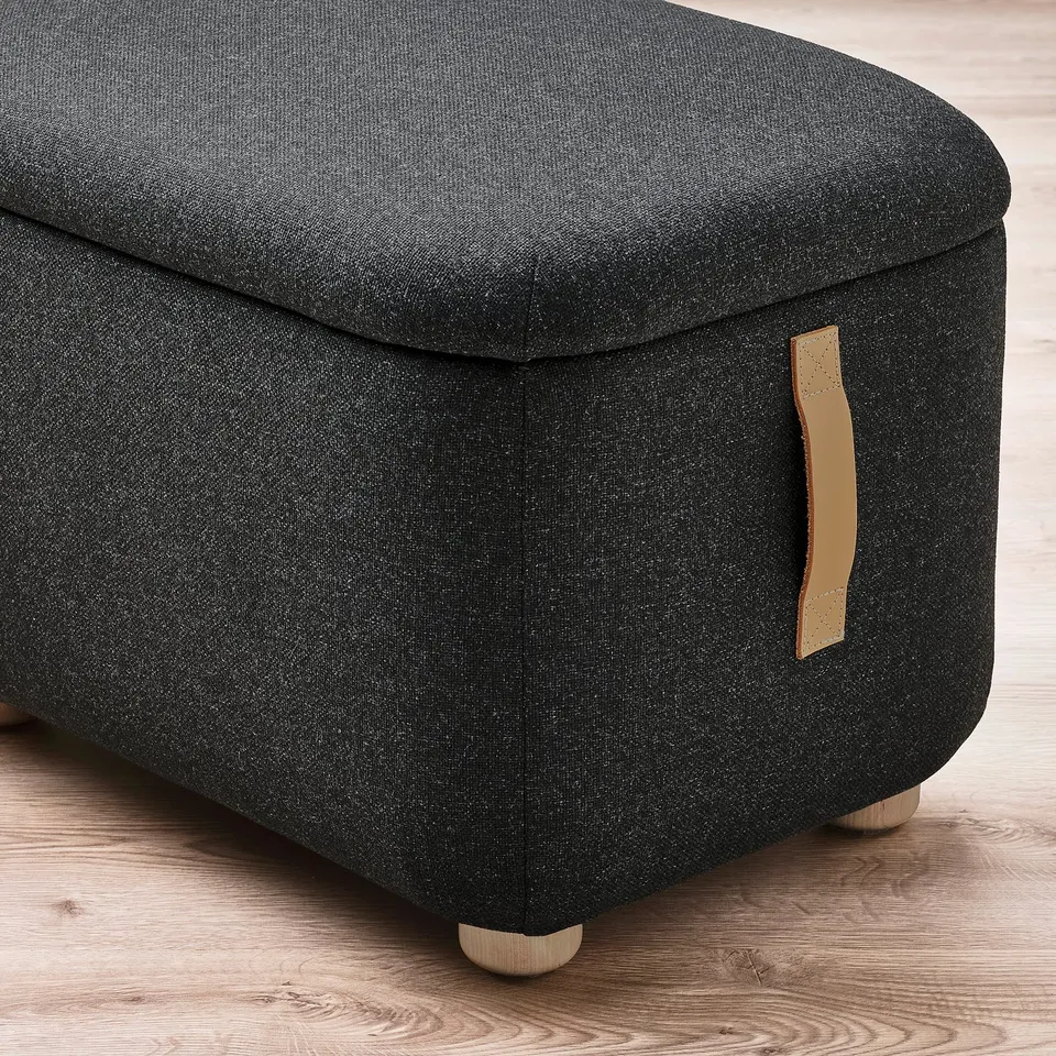 Dark grey fabric ottoman with wooden legs and leather handle.