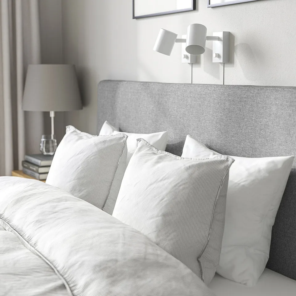 Nachdem modern white bed with soft, padded headboard. Wall-mounted lights above, two lamps on bedside table beside it.