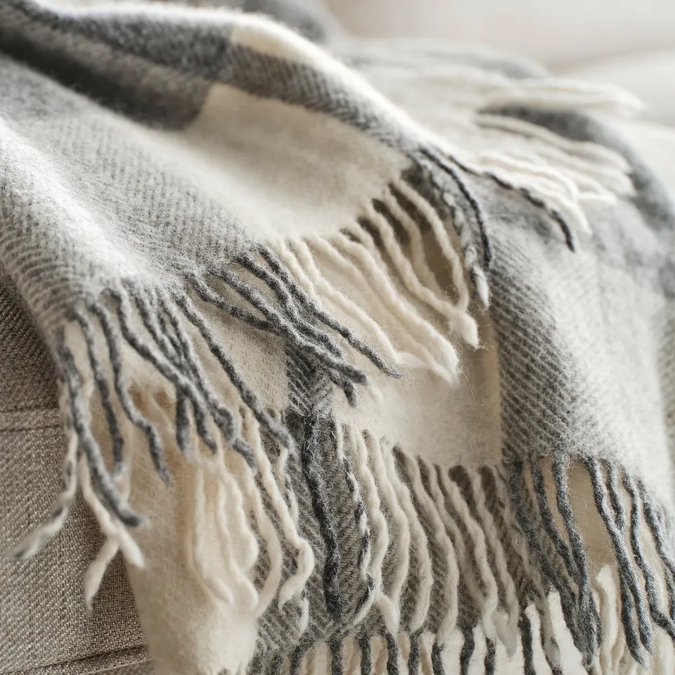 Close-up of cosy, textured wool blanket with fringe; light grey with dark stripes.