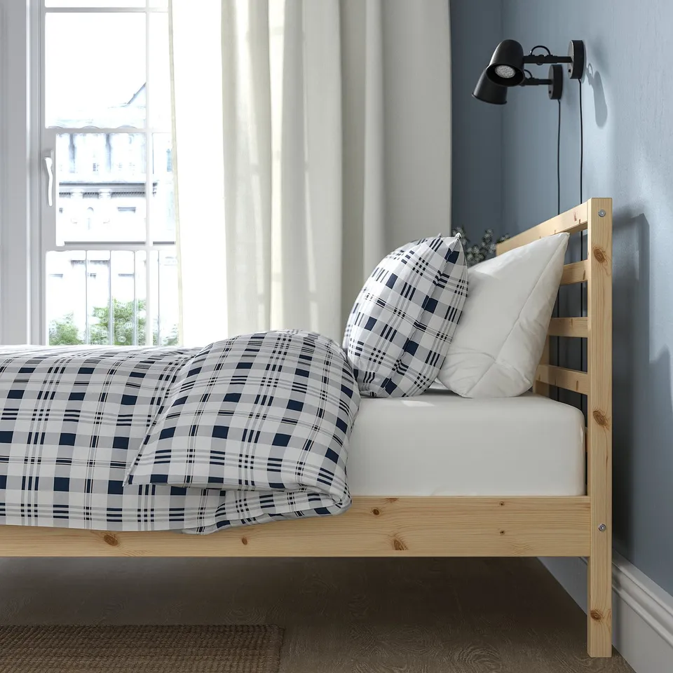 Cosy bedroom with wooden TARVA bed, plaid duvet, and wall light.