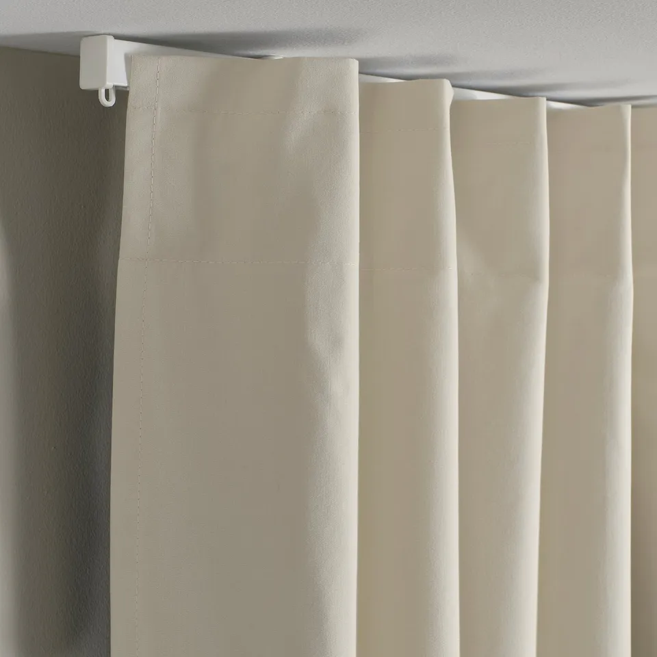 Beige curtain with wide heading tape hangs neatly from ceiling rod, blocking light.