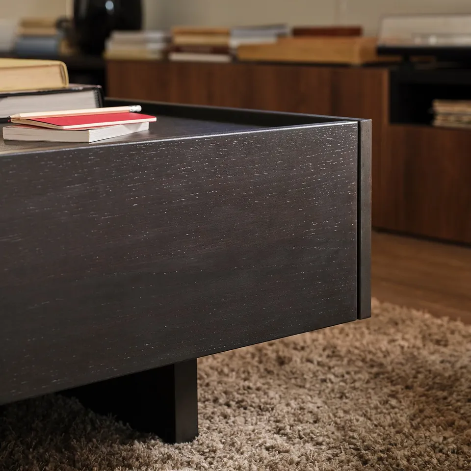 Dark wooden coffee table with visible grain texture, two red books stacked on top, and a soft textured beige rug beneath.