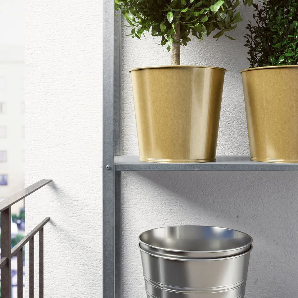 Two golden pots with green plants on a metal shelf. A large silver bin below, next to a railing.
