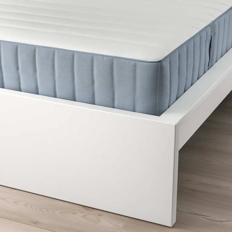 A neatly made bed with a white frame and grayish-blue mattress, showing clean, minimalist design.