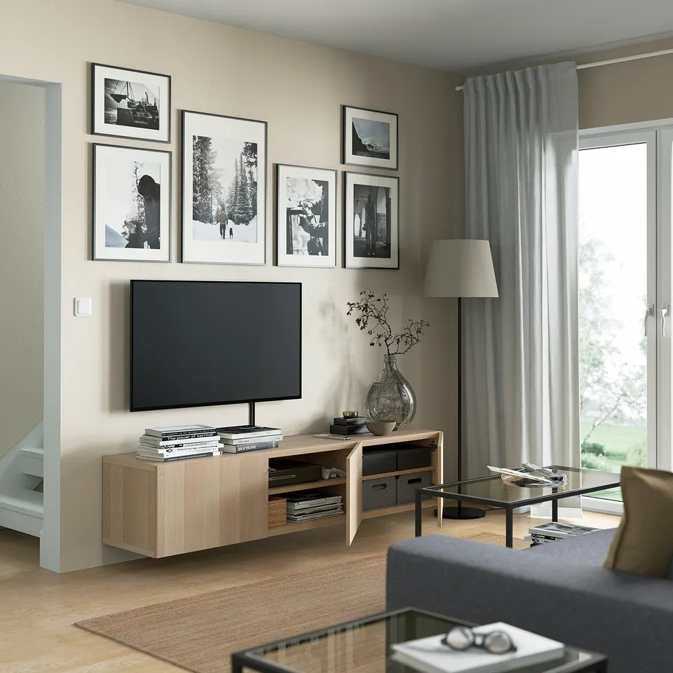 Modern living room with tv on wooden stand, framed art, grey curtains, and glass coffee table.