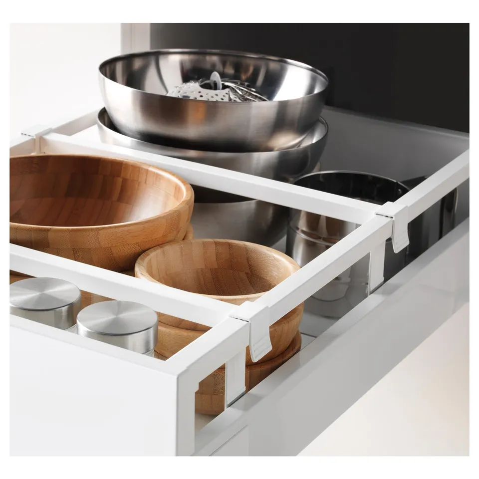White kitchen drawer with adjustable shelf holding wooden and metal bowls, organised.