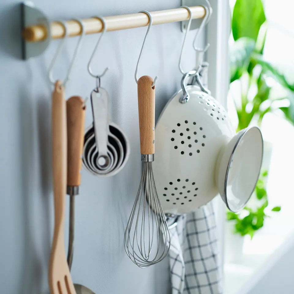 Wooden-handled kitchen tools hang from hooks on a gold rail, including a whisk, measuring cups, and a colander.