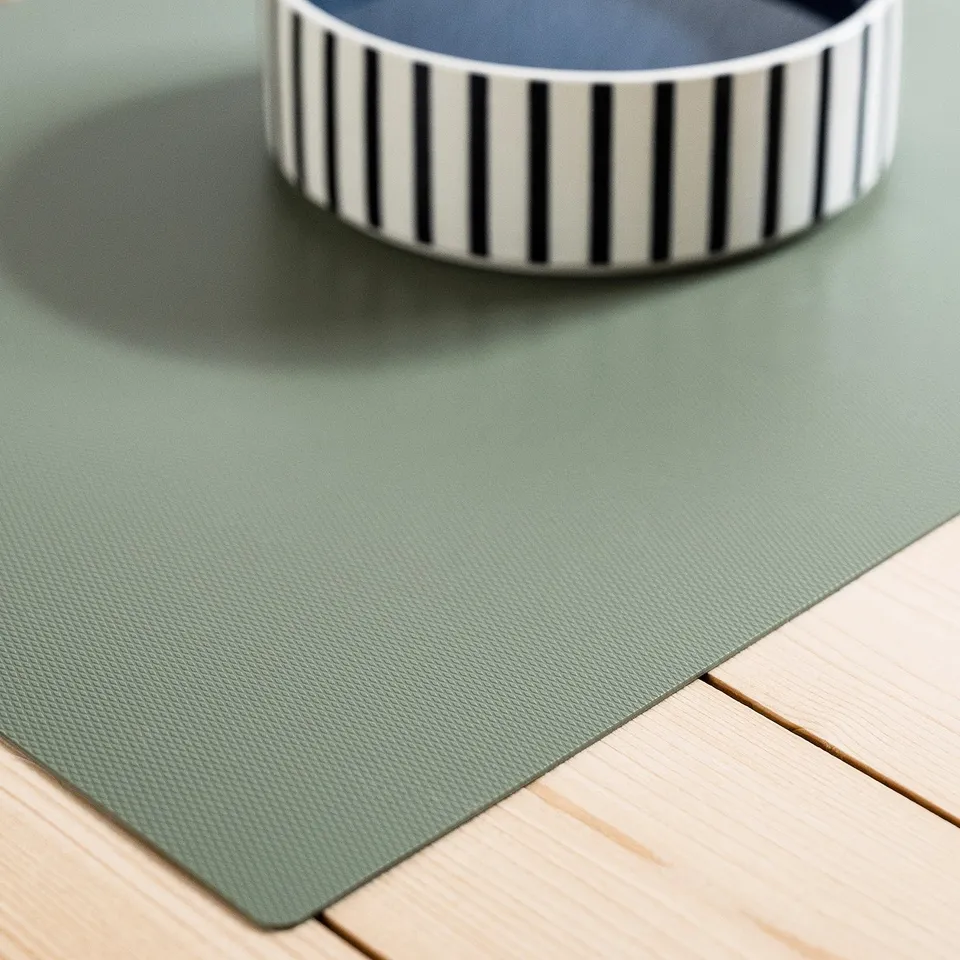 Green non-slip pet mat with striped bowl on wood floor. Protects floor and keeps bowl steady.