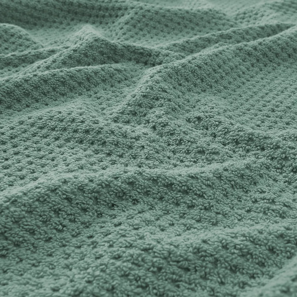 Soft, plush green towel with intricate weave, showcasing its thick, absorbent texture.