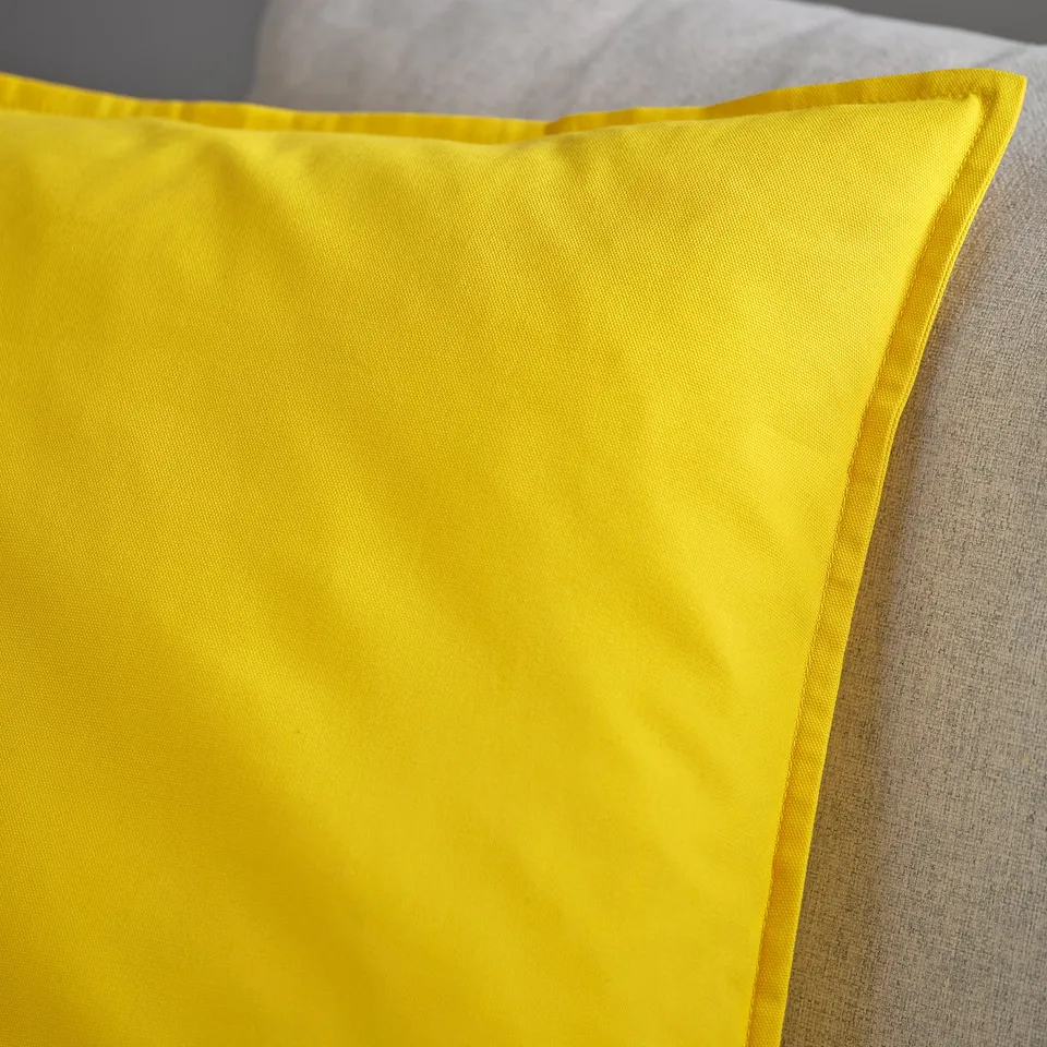 Bright yellow cushion cover made from recycled cotton, laid out smoothly on a bed, showcasing its vibrant colour and neat stitching.