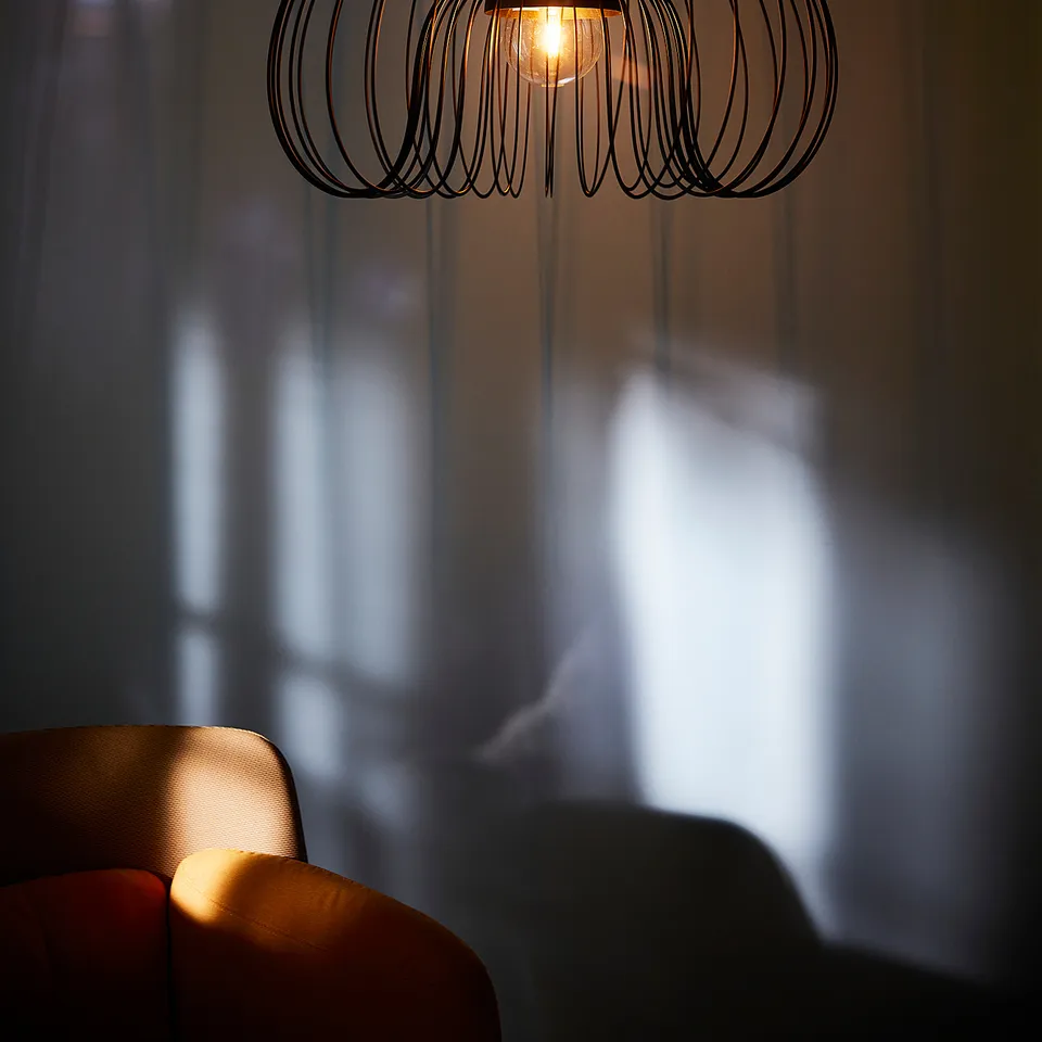 Wireframe pendant lamp hangs, casting warm light on red chair.
