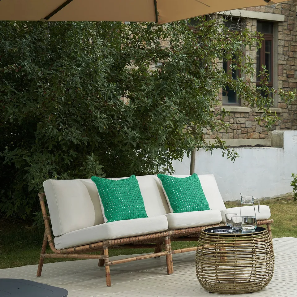 TVARÖ outdoor sofa: stylish, comfortable, natural-brown rattan with white cushions and green pillows, perfect for outdoor relaxation.