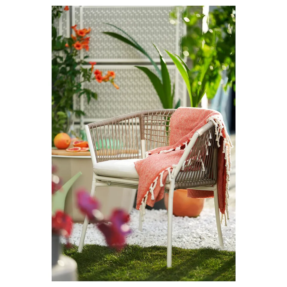Modern outdoor patio scene with woven wicker chair, orange blanket, and lush greenery.