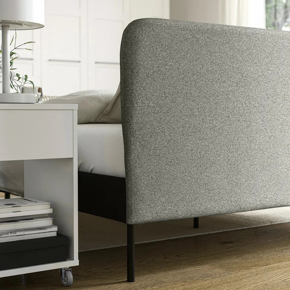 A modern bed frame with a cushioned headboard, featuring a storage shelf with books, and a lamp, ideal for a cosy bedroom.