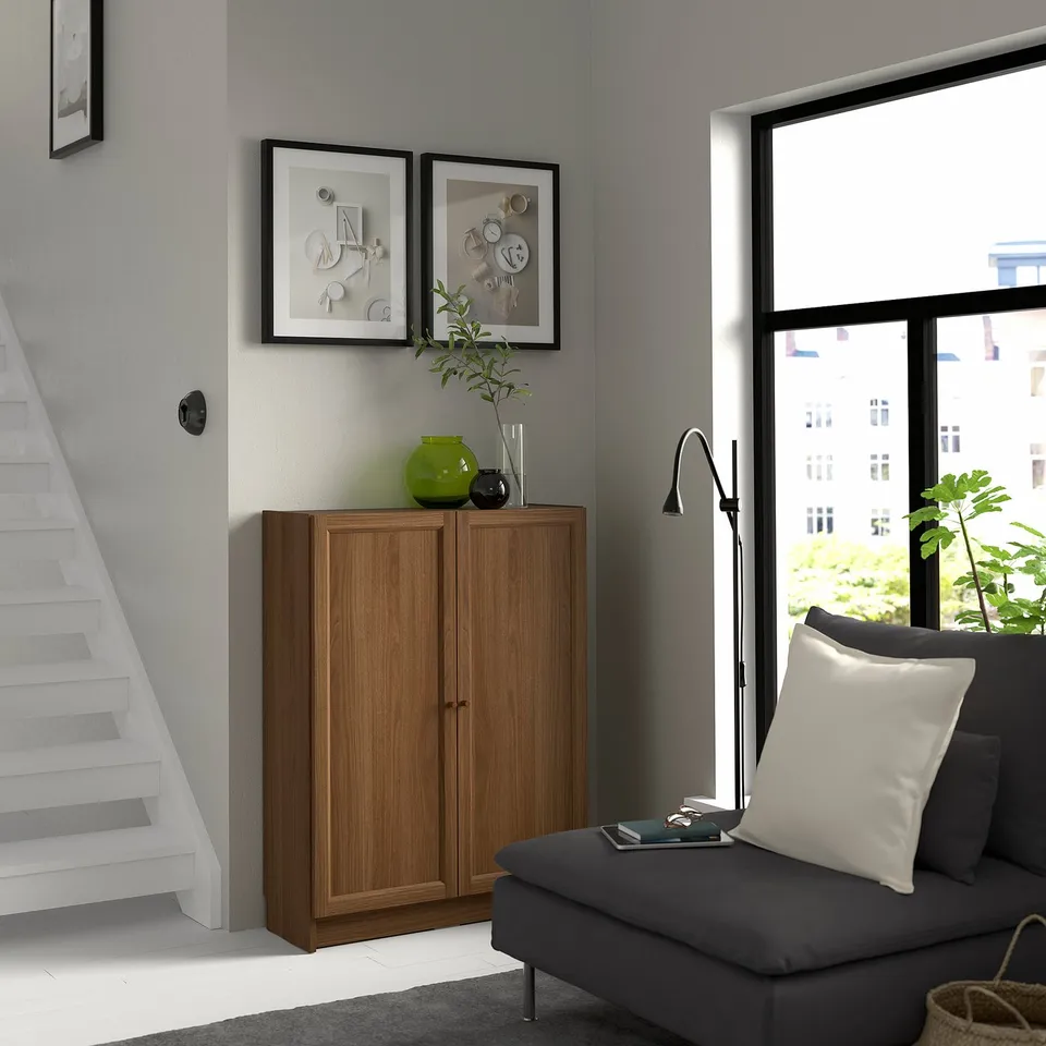 Modern living room with BILLY bookcase, grey sofa, and urban view from window.