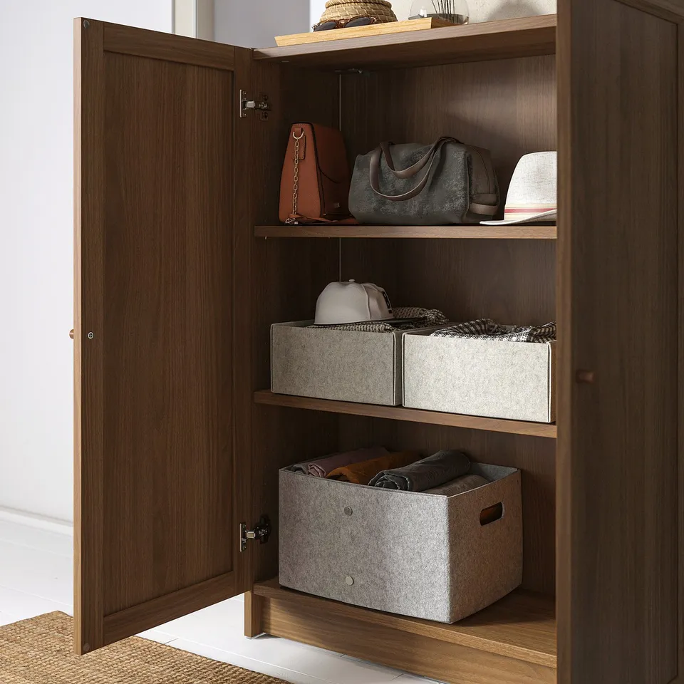 Wooden cabinet with three shelves showing storage of handbags and boxes.