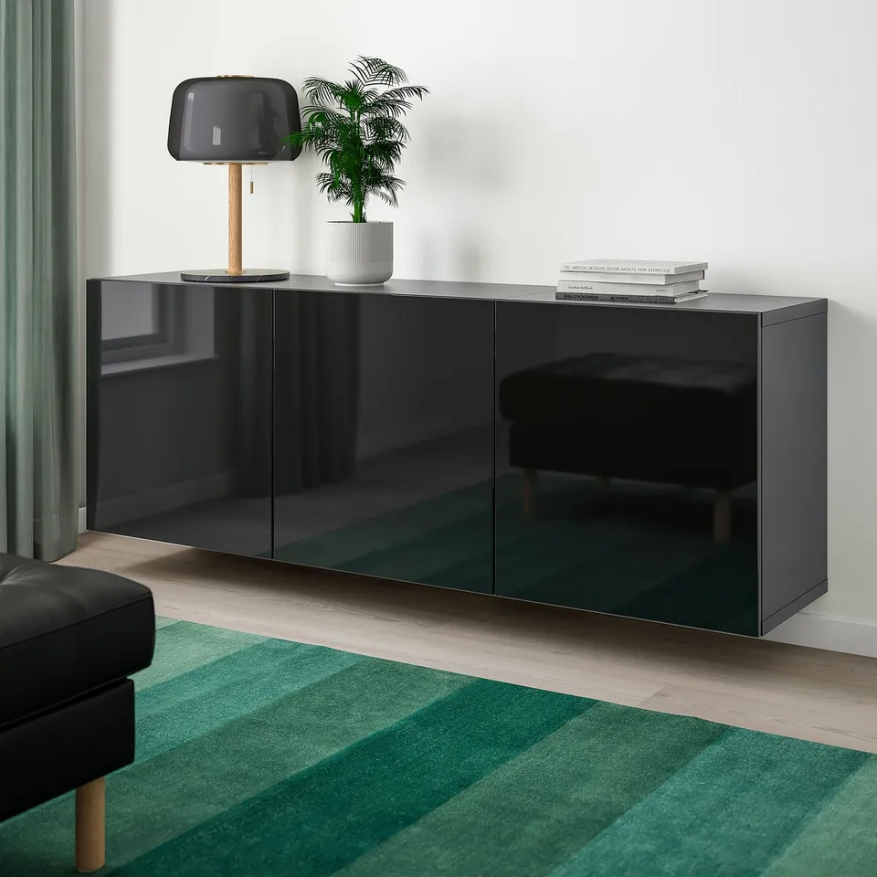 Modern black BESTÅ sideboard with glossy finish, contrasting white wall, black couch, green rug.