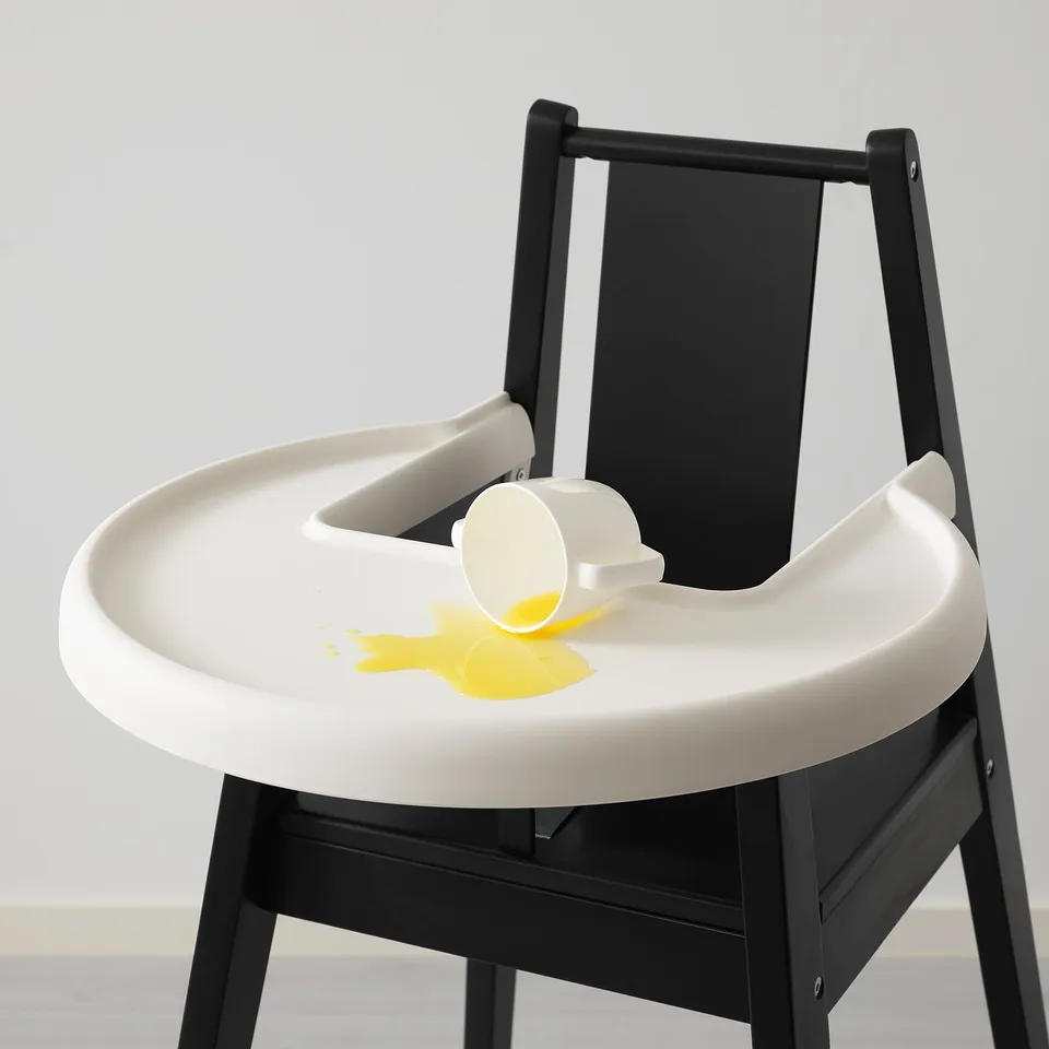 White highchair with black legs, spilled yellow liquid on tray.