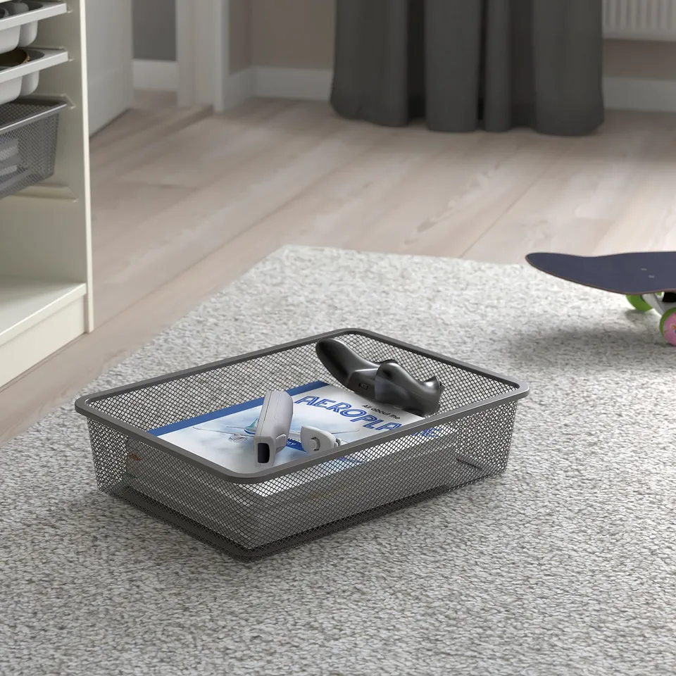 Mesh storage basket on rug with remote, book, and game controller, part of TROFAST series for organising items.
