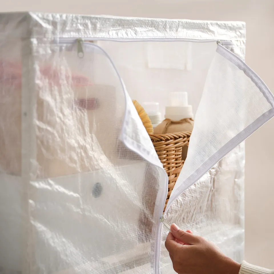 A person is opening a white, zippered, transparent storage bag containing basket and bottles.