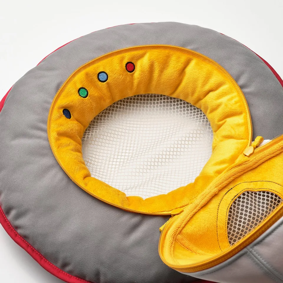 A soft, round, grey spaceship toy with a bright yellow interior. It mesh pockets and colourful embellishments inside.