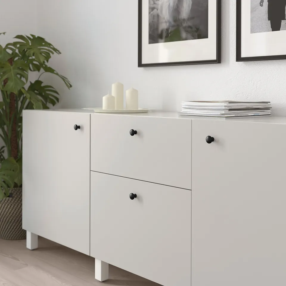 White cabinet with black knobs displays books and candles.