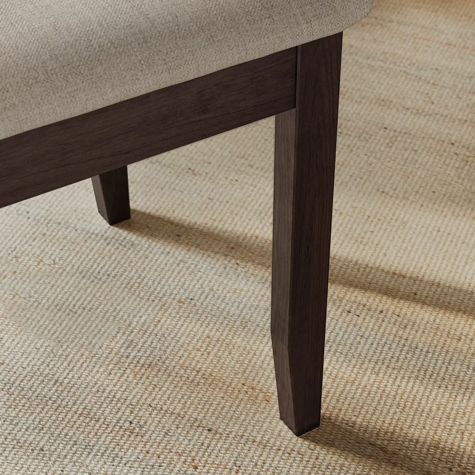 Dark wood chair leg on beige rug detail, highlighting craftsmanship.