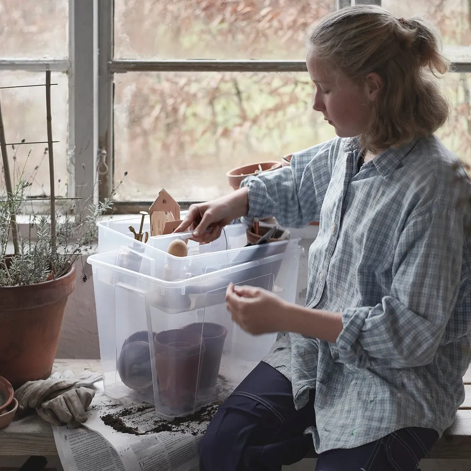 Person organising a SAMLA box with items by a window, plant, and gloves.