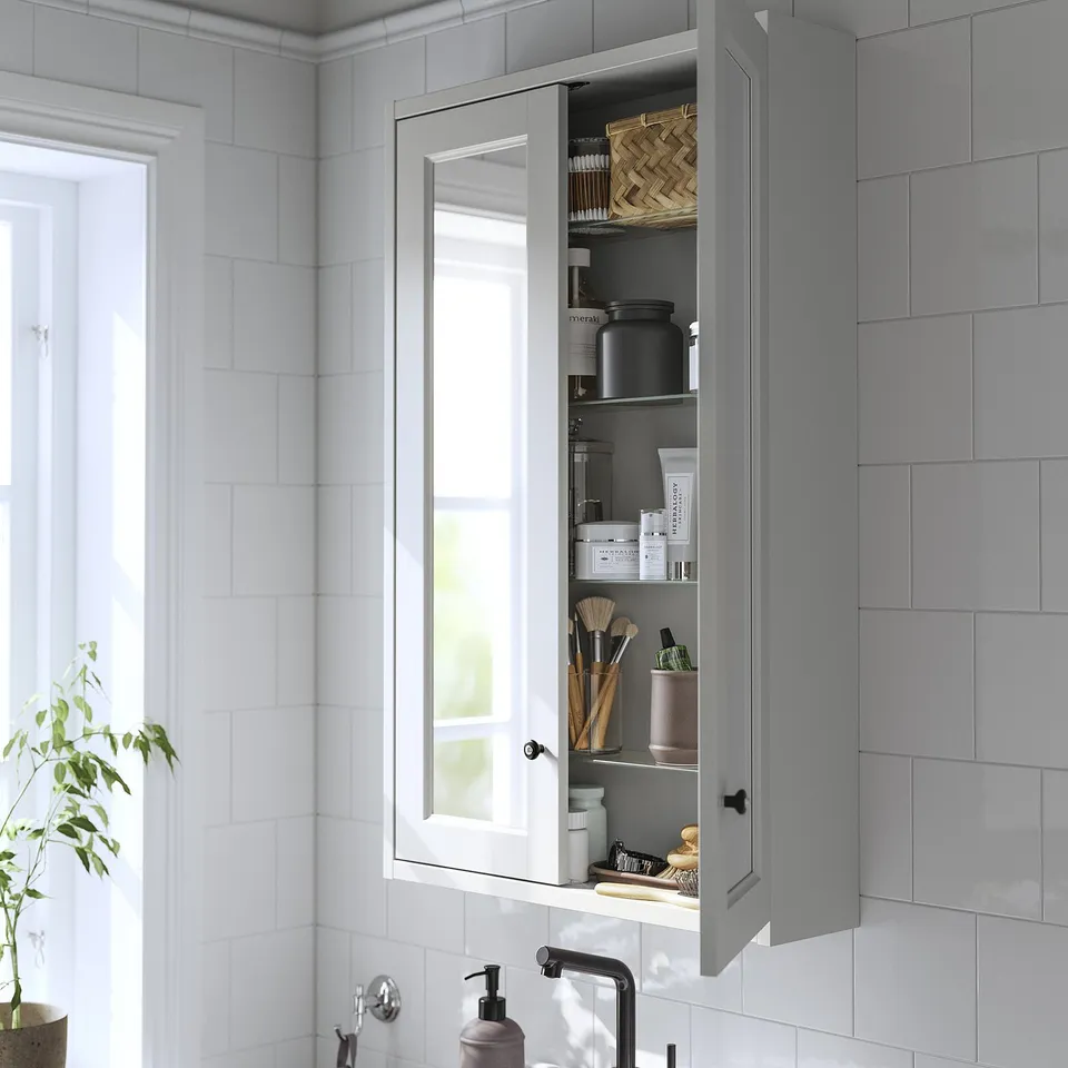 Wall-mounted grey bathroom cabinet with mirror doors open, revealing shelves stocked with toiletries and makeup.