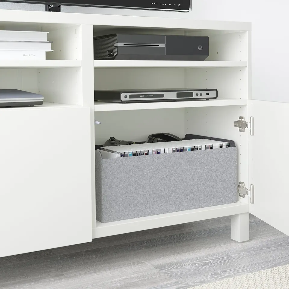 White BESTÅ tv bench with adjustable shelves, storing electronics and games, with cable management and soft-close doors.