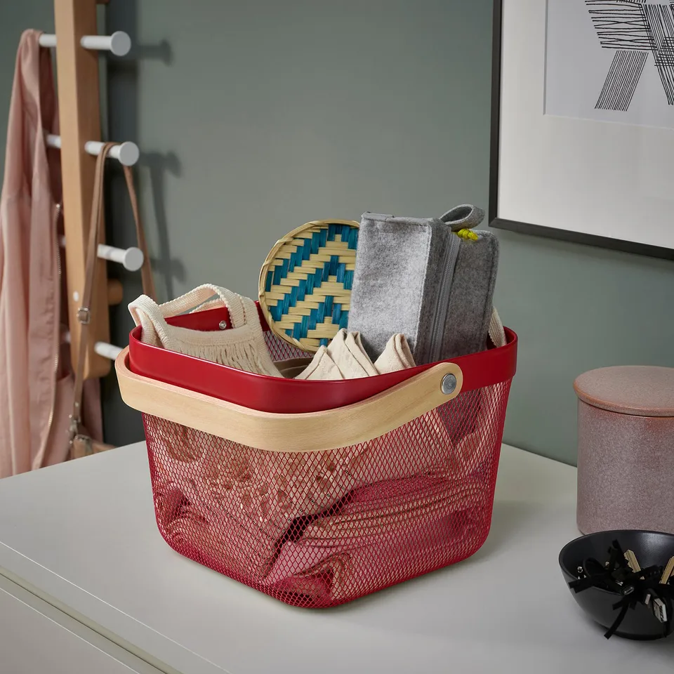 Red mesh storage basket with wooden handles holds woven tray and fabric items, ideal for organising various items indoors.