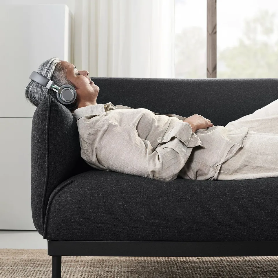 Person relaxes on ÄPPLARYD sofa with headphones. Sleek & comfy fabric cover.
