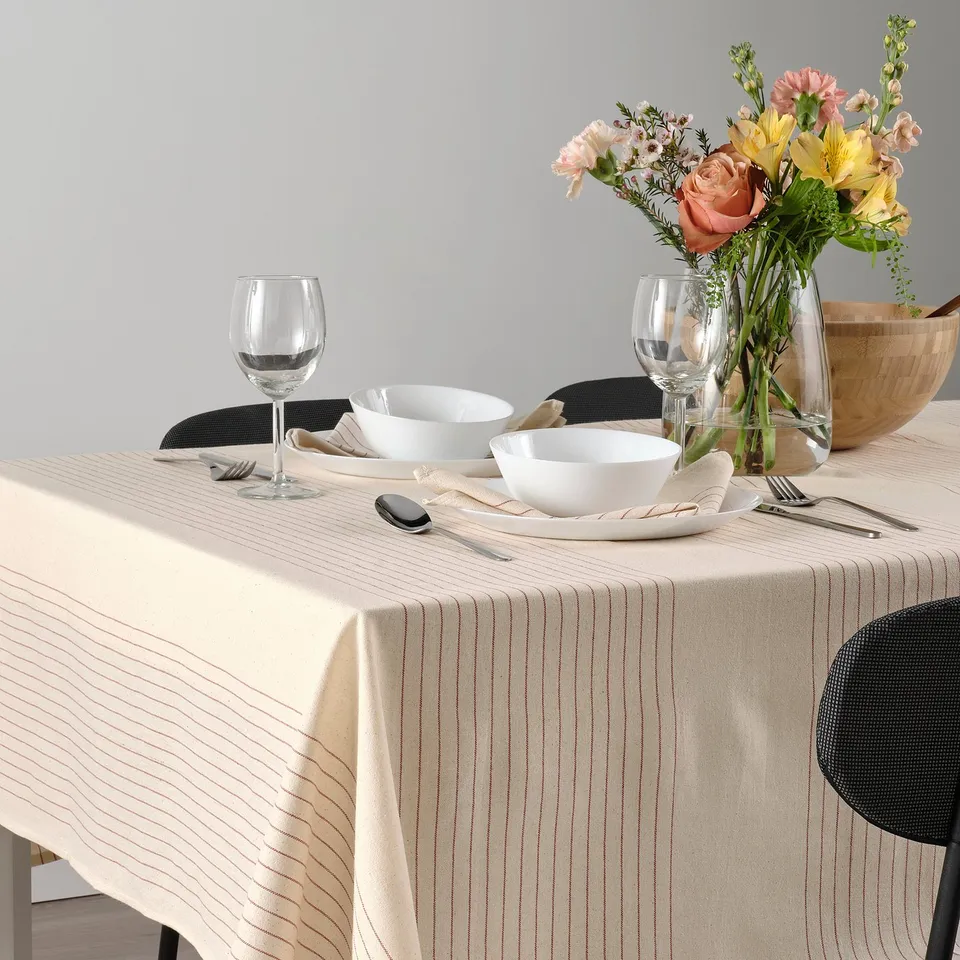 Table set with white tablecloth, bowls, glasses, cutlery, and flowers in vase.